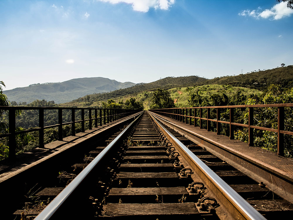 View of train tracks lined towards a horizon with hills and blue sky